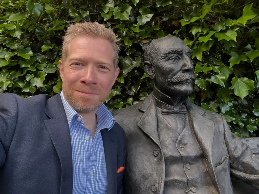 Zeb smiling and sitting next to a statue of Elgar